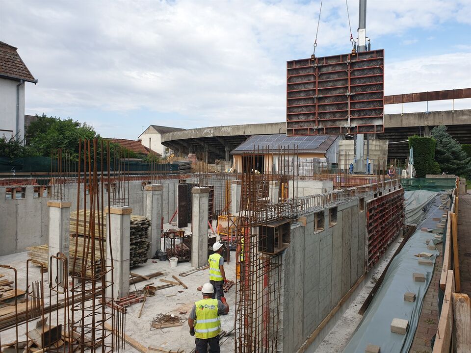 Clinica Datcu din Satu Mare, în execuție: pereții și stâlpii subsolului din beton armat, decofrați, cu un panou de cofraj ridicat de macara și echipa Civila pe șantier