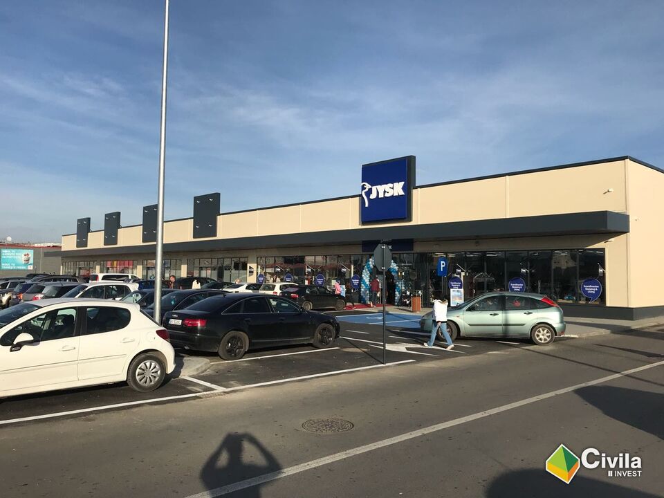 Centrul comercial din Făgăraș, pentru PK Red: magazinele cu vitrine sub copertina continuă, baloane la intrarea unui magazin și parcarea plină de mașini