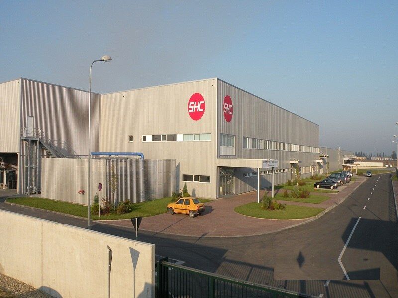 Fabrica ShinHeung Electronics din Oradea, finalizată: hala cu sigla SHC, intrarea cu copertină, spațiile verzi și aleea de acces cu parcarea