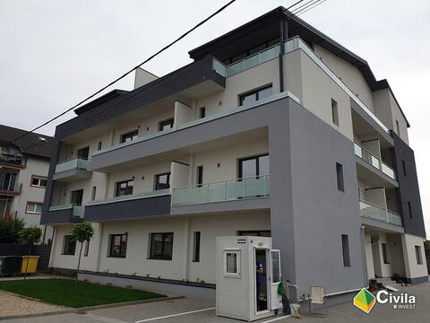 Blocul P+3 din Timișoara terminat, cu fațadele albe și gri, balcoanele cu parapete din sticlă și gazonul din fața lui