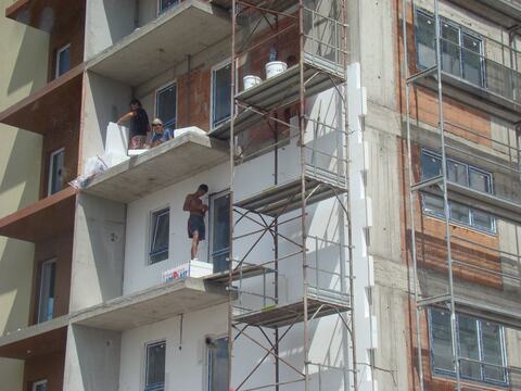 Montajul plăcilor termoizolante pe fațada blocului A5, de pe schelă și de pe balcoane; alături, zidăria din cărămidă încă neizolată