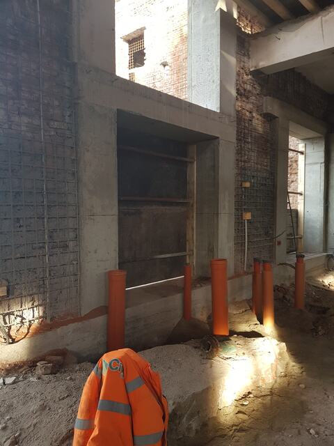 Pereți armați cu plasă și cadre noi din beton în jurul golurilor, cu țevi portocalii la baza pereților