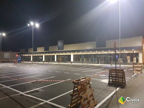 Centrul comercial din Făgăraș seara, cu parcarea încă goală, marcată și iluminată; în față, paleți și bandă de avertizare