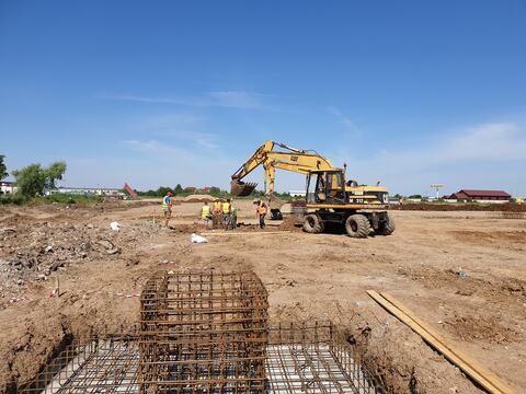 Excavatoare și echipa la lucru între gropile de fundație, lângă carcase de armătură, cu o fundație armată în prim-plan, la șantierul Hornbach din Oradea