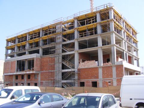 Clădire cu mai multe niveluri în execuție: cadre din beton armat, cofraje de planșeu la nivelurile de sus și zidărie la etajele de jos
