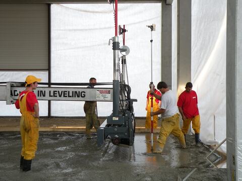 Turnarea unei pardoseli industriale: echipa nivelează betonul proaspăt cu o mașină de nivelare și o miră