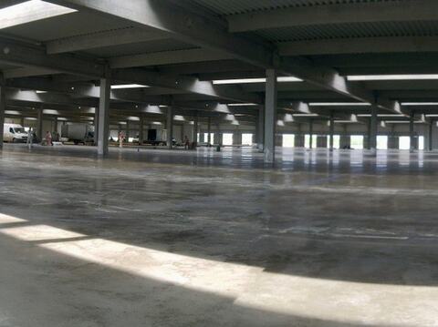 Pardoseala industrială gata într-o hală mare cu structură prefabricată, luminată de soare, cu vehicule și oameni în fundal