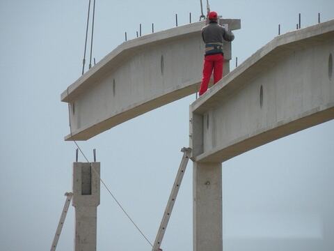 Montajul unei grinzi prefabricate din beton: grinda coborâtă cu macaraua pe capul stâlpului, cu montatorul deasupra