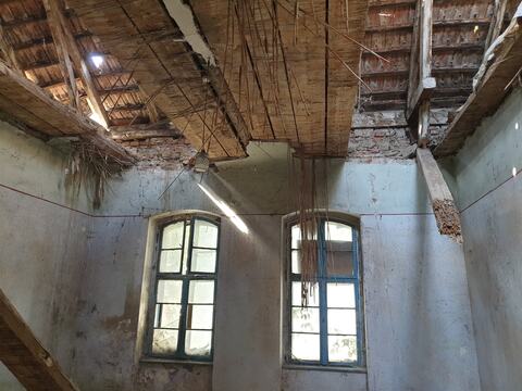Interior degradat, cu tavanul desprins, grinzile de lemn la vedere și tâmplăria veche pe loc