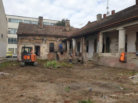 Curtea casei la începerea lucrărilor, cu un miniexcavator și corpurile vechi în jur