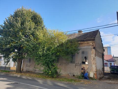 Corpul vechi al casei spre stradă, acoperit cu plasă de protecție, cu doi muncitori la colțul clădirii