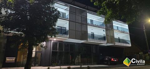 Fațada clădirii New City văzută din unghi, seara: balcoanele iluminate, panourile perforate și parterul vitrat