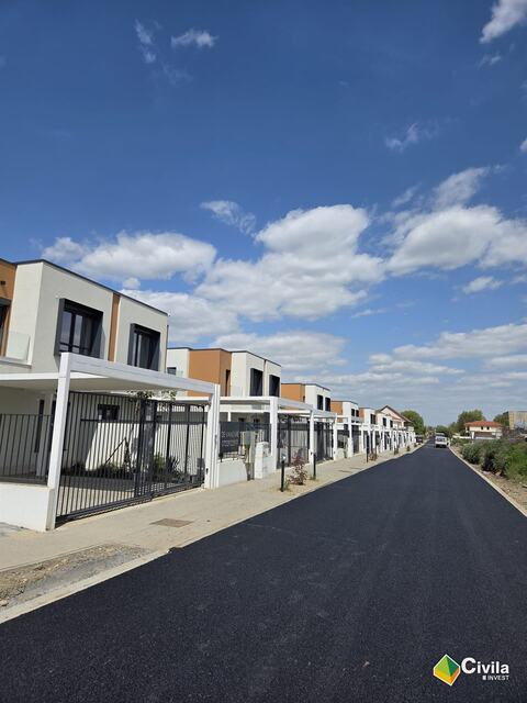 Strada din Royal Valley, cu asfaltul nou, trotuarul pavat și porțile duplexurilor sub pergolele albe de la stradă