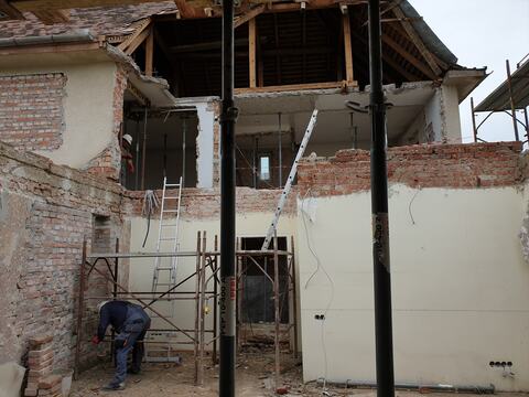 Casa veche deschisă spre curte: planșeul de la etaj sprijinit pe popi metalici, pereții de la parter desfăcuți parțial și șarpanta la vedere