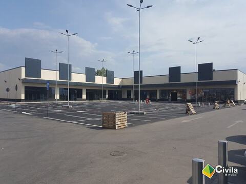 Centrul comercial din Târgu Secuiesc, finalizat: fațada lungă cu vitrine sub copertină și parcarea marcată, încă goală