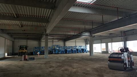 Interiorul centrului comercial, cu grinzile prefabricate, acoperișul din tablă, un cilindru compactor și nacelele parcate